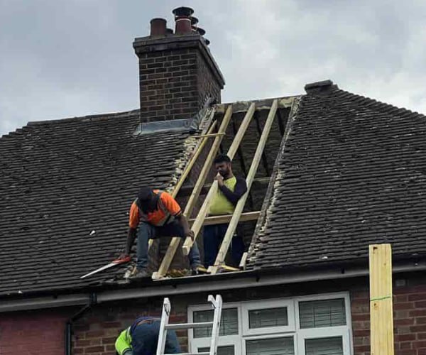 This is a photo of a roof repair being carried out. A section of the roof has been stripped and two roofers are replacing the rafters. Works being carried out by NRS Roofing Thrapston